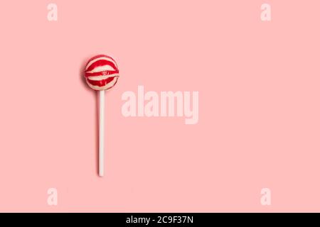 Un lollipop rosso e bianco su sfondo rosa con spazio di copia Foto Stock