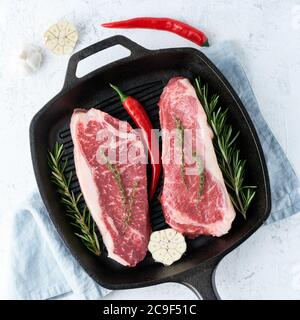 Due pezzi interi grezzi freschi, filetto di manzo, striploin di marmo in grande padella di ghisa Foto Stock