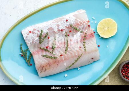 Filetto di pesce bianco crudo di walleye su un piatto blu su sfondo bianco. Pezzo intero di pesce fresco Foto Stock