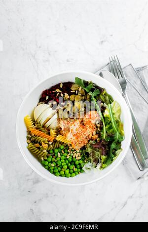 Una ciotola sana per il pranzo. Pollo, fusilli di pasta, capperi, verdure miste, verdure e semi di girasole. Delizioso concetto di cibo bilanciato. Vista dall'alto, disposizione piatta, c. Foto Stock