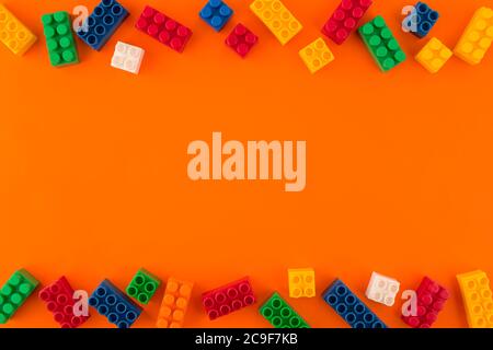 Pile di blocchi di plastica colorati e di mattoni colorati su sfondo arancione. Spazio di copia. Vista dall'alto. Foto Stock