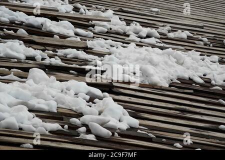Grumi di ghiaccio e neve sulla cima di un vecchio tetto di legno. Neve bianca chiara in contrasto con le lunghezze scure del legno. Foto Stock