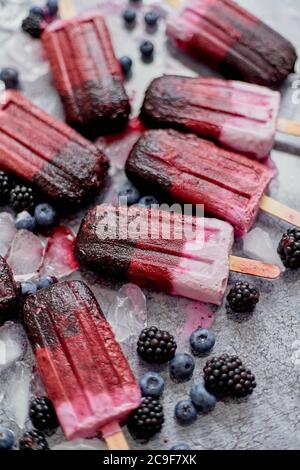 frullato e gelati o popsicle fatti in casa con bacche surgelate su vassoio di ardesia nero Foto Stock