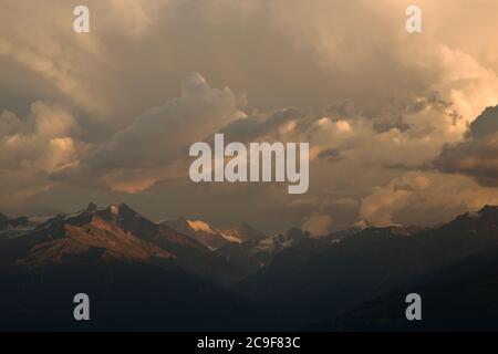 Nuvole scure e epiche sopra un paesaggio montano spettacolare. Sole che colpisce le cime della montagna. Dorata, luce da sera. Foto Stock