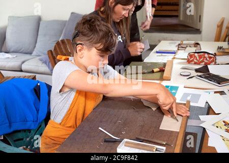 Bambino con impianto cocleare imparare ad usare lo strumento di linocut mentre si stampano in un laboratorio di classe d'arte in Carmarthenshire Galles UK KATHY DEWITT Foto Stock