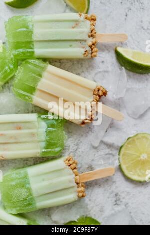 Lime e panna fatta in casa popsicles o gelati messi con cubetti di ghiaccio su sfondo di pietra grigia Foto Stock
