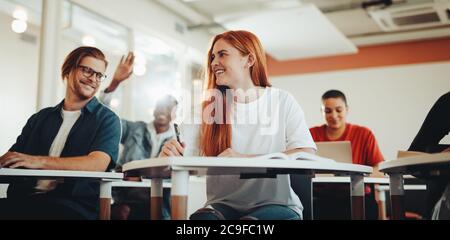 Studenti di sesso maschile e femminile che parlano in classe durante la lezione. Gli studenti sorridono e discutono in conferenza. Foto Stock