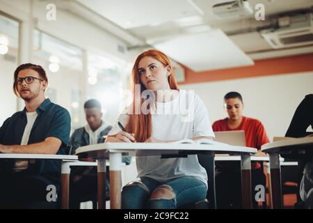 Piuttosto studente adolescente prestando attenzione alla lezione in aula. Donna che studiano al Collegio in aula. Foto Stock