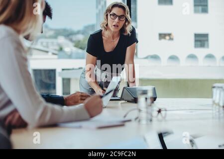 Donna che spiega nuove strategie ai colleghi durante la riunione. Uomini d'affari che si riunano nella sala del consiglio d'amministrazione per la discussione di nuovi progetti. Foto Stock