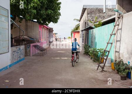 Bodufolhudhoo / Maldive - 17 agosto 2019: Maldivian ragazzo in bicicletta sulla strada sabbiosa in Maldive città isola con il mare in background Foto Stock