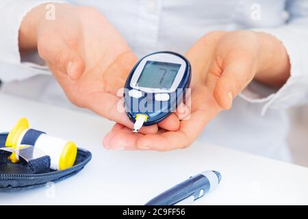 Le mani della donna che tengono il tester del diabete nei palmi che mostrano i risultati Foto Stock