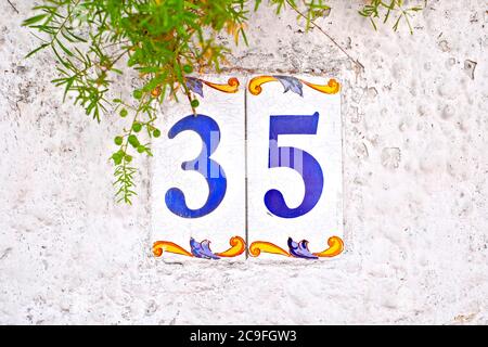 Trentacinque, numero 35, piastrelle numerate decorative con elemento floreale su parete bianca. Foto Stock