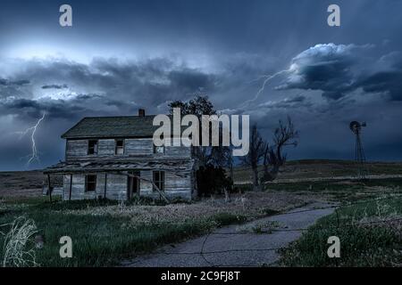 Una lunga esposizione di una vecchia casa infestata, dilapidata nella rurale Midwest di notte, incorniciata da inquietanti cieli scuri e fulmini. Foto Stock