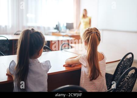 Due piccole studentesse si siedono su una scrivania in una classe scolastica e ascoltano attentamente l'insegnante Foto Stock