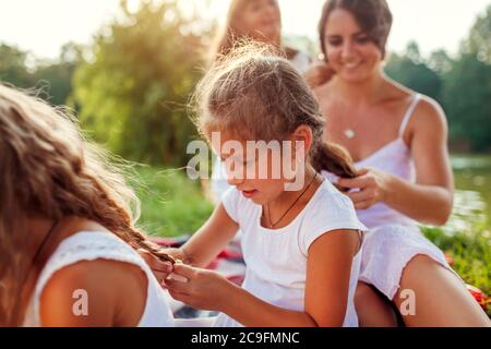 Madre, nonna e capretti tessono le trecce l'una all'altra. La famiglia si diverte durante il picnic nel parco estivo. Foto Stock