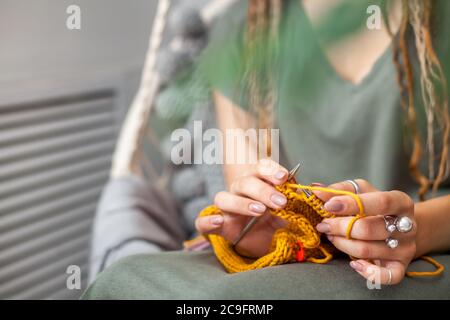 Primo piano delle mani femminili con maglia. Aghi per maglieria in metallo. Tessuto a maglia giallo. Foto Stock