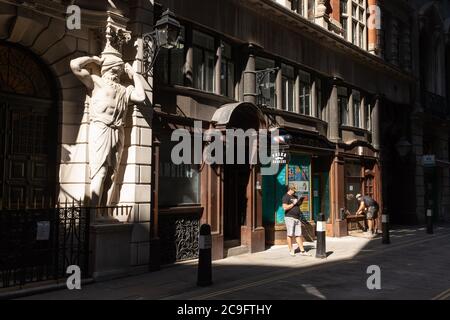 Due operai stanno vicino alla figura di Atlantes dallo scultore H. A. Pegram (1896) all'entrata della compagnia di livrea di Draper' Hall in Throgmorton Street, un guardiano si stema per raccogliere le chiavi cadute fuori dalla Drapers Hall in Throgmorton Street, nella città di Londra, Il 30 luglio 2020, a Londra, Inghilterra, è il quartiere finanziario della capitale, detto anche Square Mile. La Compagnia dei rapitori è una Livery Company nella città di Londra le cui radici risalgono al XIII secolo, quando, come indica il nome, era coinvolta nel commercio dei tendaggi. (La descrizione continua in ulteriori informazioni). Foto Stock