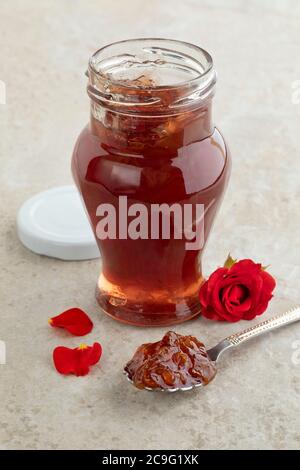 Vaso di vetro con marmellata fatta in casa di petali di rosa e una rosa rossa fresca Foto Stock