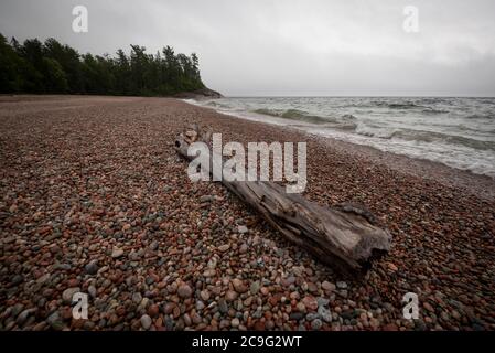 Un tronco di driftwood si trova in cima a una spiaggia sassosa e spazzata dal vento sulla riva settentrionale del lago Superior. Foto Stock