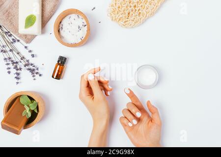 Le mani femminili applicano la crema accanto ai cosmetici naturali e gli accessori zero rifiuti sul tavolo bianco, vista dall'alto. Foto Stock