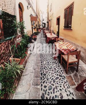 Pittoresco vicolo con tavoli e sedie nel centro storico di Castelsardo, Italia Foto Stock
