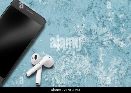Cuffie o auricolari bluetooth wireless bianchi, smartphone con texture blu, primo piano Foto Stock