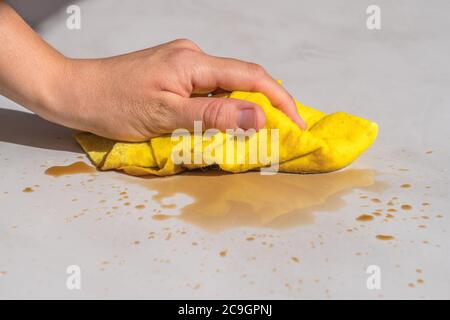la macchia di tè per la pulizia delle mani della donna o il caffè versato su un pavimento di cemento con un panno giallo per il pavimento per la pulizia delle stoviglie Foto Stock