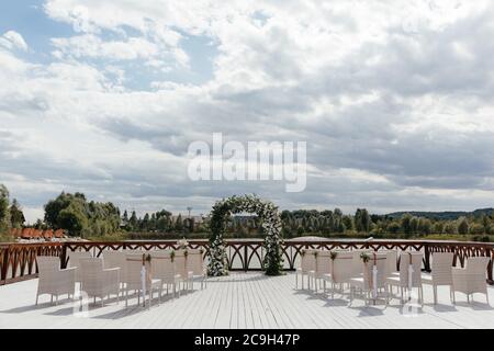 Luogo della cerimonia nuziale. Sedie bianche per gli ospiti alla cerimonia nuziale e arco di nozze Foto Stock