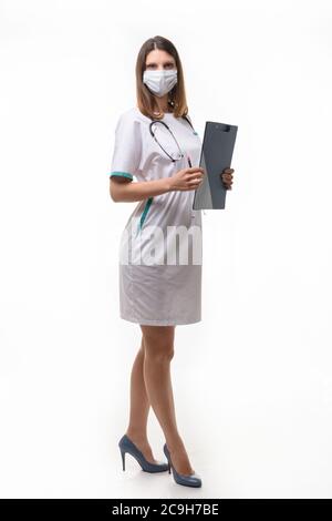 ragazza medico in abiti medici e maschera con compressa in mano su sfondo bianco si sviluppa in piena crescita Foto Stock