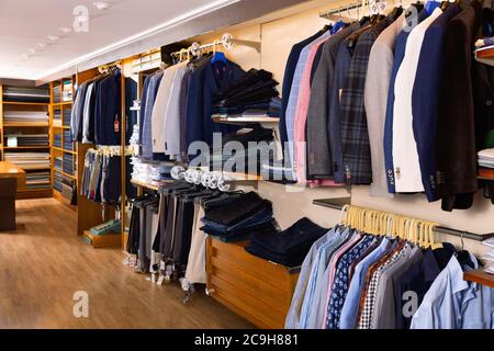 Moda uomo moderno moda abiti esposti su scaffali e appendiabiti in negozio di abbigliamento Foto Stock