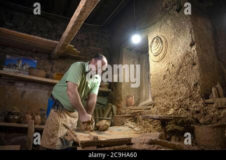 Uomo scultore che crea scultura da argilla in officina. Processo di fare una figura di creta. Uomo anziano attento che moulding creta Foto Stock