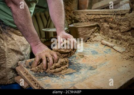 Uomo scultore che crea scultura da argilla in officina. Processo di fare una figura di creta. Uomo anziano attento che moulding creta Foto Stock