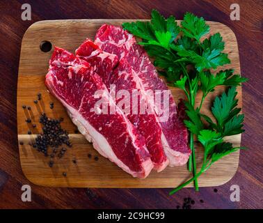 Carni fresche di manzo marmorizzate a fette con prezzemolo e condimenti preparati per la tostatura su tavola di legno Foto Stock