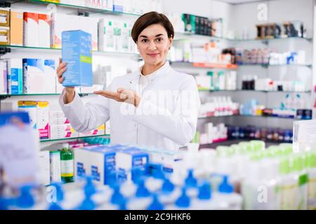 Giovane femmina allegro farmacista suggerendo utili prodotti per la cura del corpo in farmacia Foto Stock