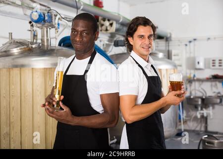 Due produttori professionali che mostra il vetro e il pallone di birra nella fabbrica di birra Foto Stock