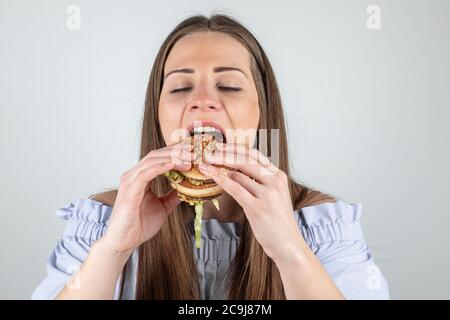 Ritratto di una bella giovane donna che mangia un hamburger, primo piano, occhi chiusi, isolato su sfondo bianco Foto Stock