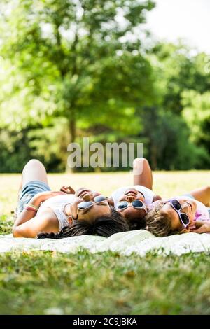 Ragazze che indossano occhiali da sole e che si trovano fianco a fianco sulla coperta nel parco. Foto Stock