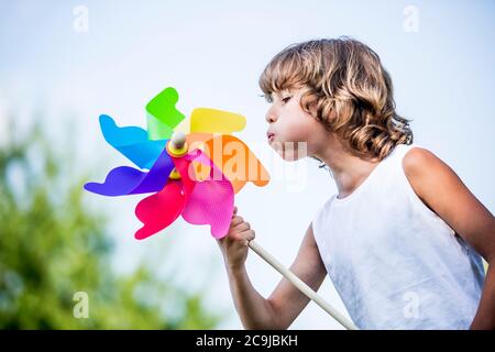 Ragazzo soffiando colorato mulino a vento di carta nel parco. Foto Stock