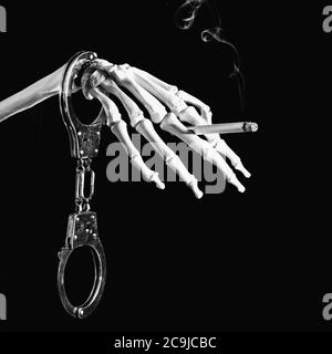 Il fumo è coinvolgente e mortale. Concetto chiaro e semplice con manette, scheletro e sigaretta bruciante. Immagine in bianco e nero su sfondo nero. Foto Stock