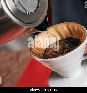 Filtrare il caffè. Versando l'acqua bollente dal bollitore nel gocciolatore manuale del caffè. Foto Stock