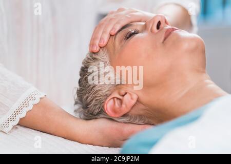 Marma terapia. Donna anziana sdraiata sul tavolo da massaggio e che gode di trattamento viso Ayurveda. Foto Stock