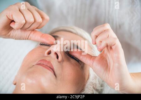 Marma terapia. Donna anziana sdraiata sul tavolo da massaggio e che gode di trattamento ayurveda occhio (Urdhaw e Adhoakshi). Foto Stock