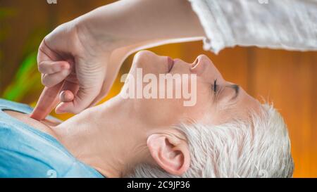 Marma terapia. Donna anziana sdraiata sul tavolo da massaggio e che gode del trattamento del collo Ayurveda. Kanth Marma. Foto Stock