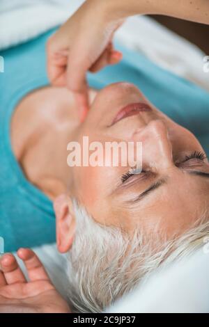 Marma terapia. Donna anziana sdraiata sul tavolo da massaggio e che gode del trattamento del collo Ayurveda. Kanth Marma. Foto Stock