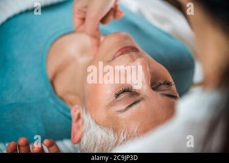 Marma terapia. Donna anziana sdraiata sul tavolo da massaggio e che gode del trattamento del collo Ayurveda. Kanth Marma. Foto Stock