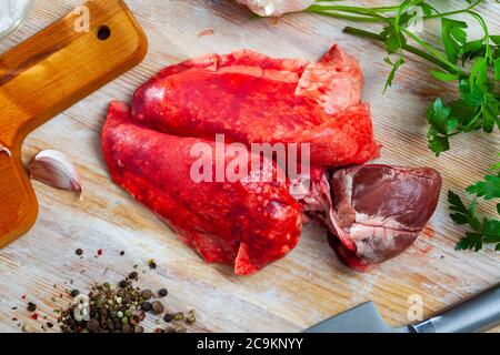 Frattaglie di montone fresche, polmoni e cuore, su fondo di legno con prezzemolo, aglio e cipolla Foto Stock