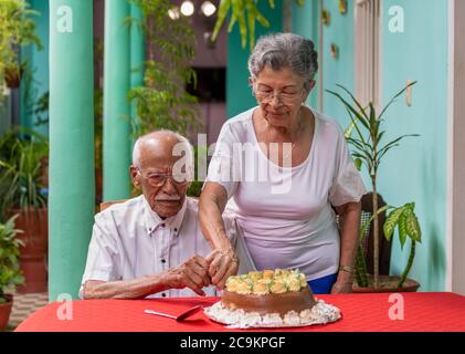 Sorridente coppia anziana tagliando una torta aiutandosi a vicenda Foto Stock