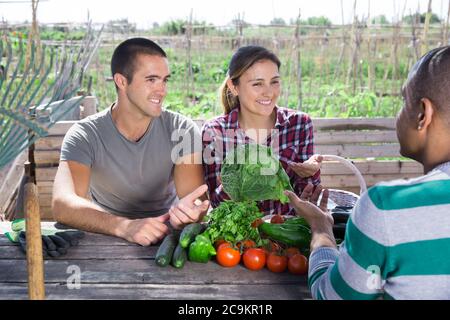 Conversazione con il vicino. Felice coppia di giardinieri dilettanti Breezily che chiacchiera con l'amico mentre sedendo al tavolo di legno all'aperto Foto Stock