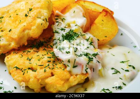 Vista ravvicinata del filetto di carne di pollo macinato con spicchi di patate fritte e salsa cremosa con pancetta su un tavolo di legno bianco Foto Stock