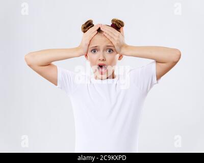 Ragazza che tiene la testa emozioni sorpresa bocca aperta t-shirt bianca spaventato espressione Foto Stock